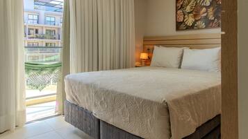 Habitación de hotel con cama, cortinas, mesita de noche con lámpara, pared con diseño de hojas y vista a un edificio.