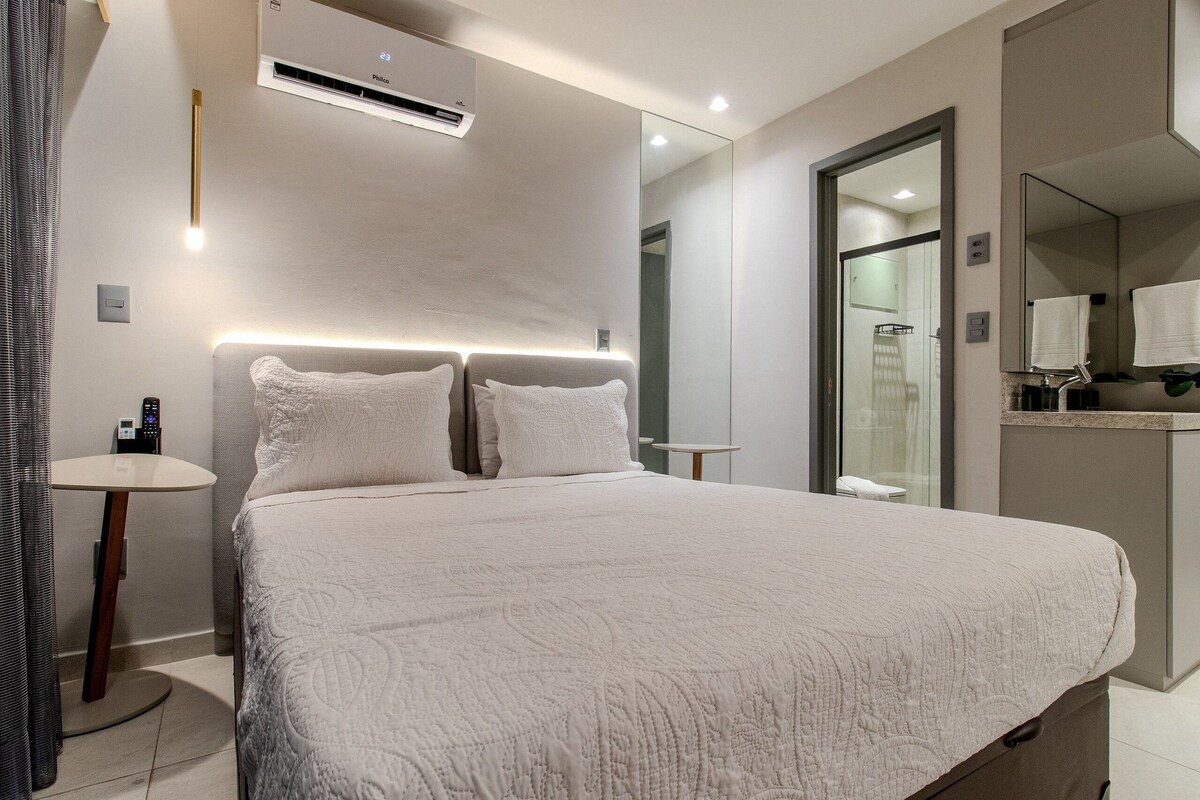 Una habitación de hotel moderna con una cama grande, mesitas de noche, un espejo y una pequeña mesa redonda.