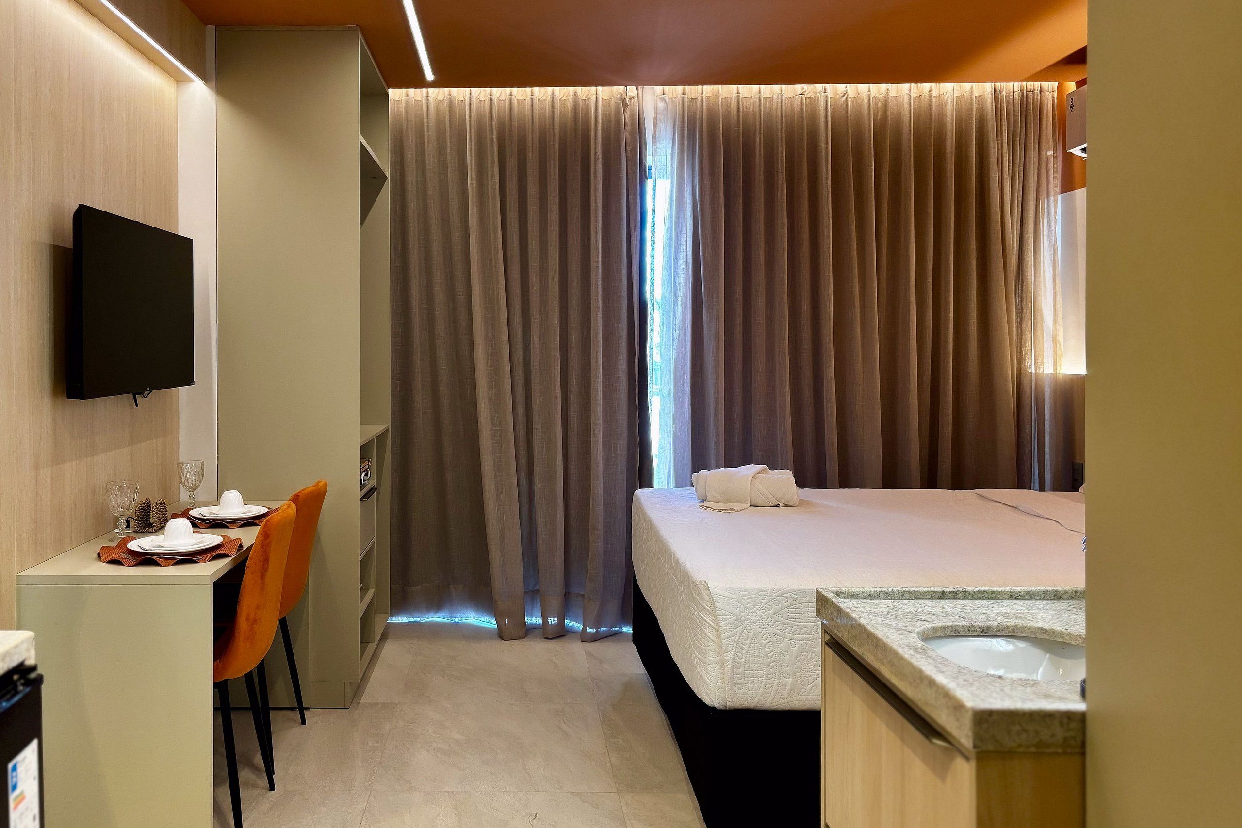 A hotel room with a bed, a desk with a chair, a television, and a window with curtains.