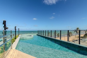 Vista despejada de una piscina con barrera de vidrio, una playa y palmeras al fondo.