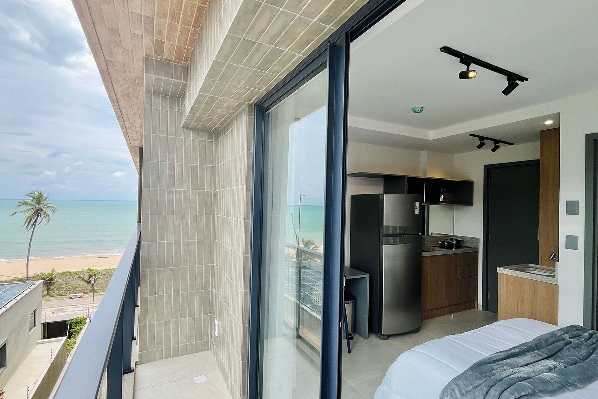 Una habitación de hotel moderna con balcón y vistas a la playa, una zona de cocina y una cama.