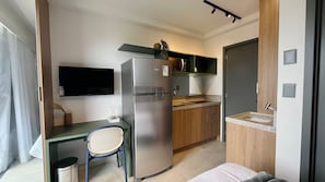 A compact kitchenette with a refrigerator, microwave, and sink, a small dining table with a chair, and a TV mounted on the wall. - Garden Haus (João Pessoa)