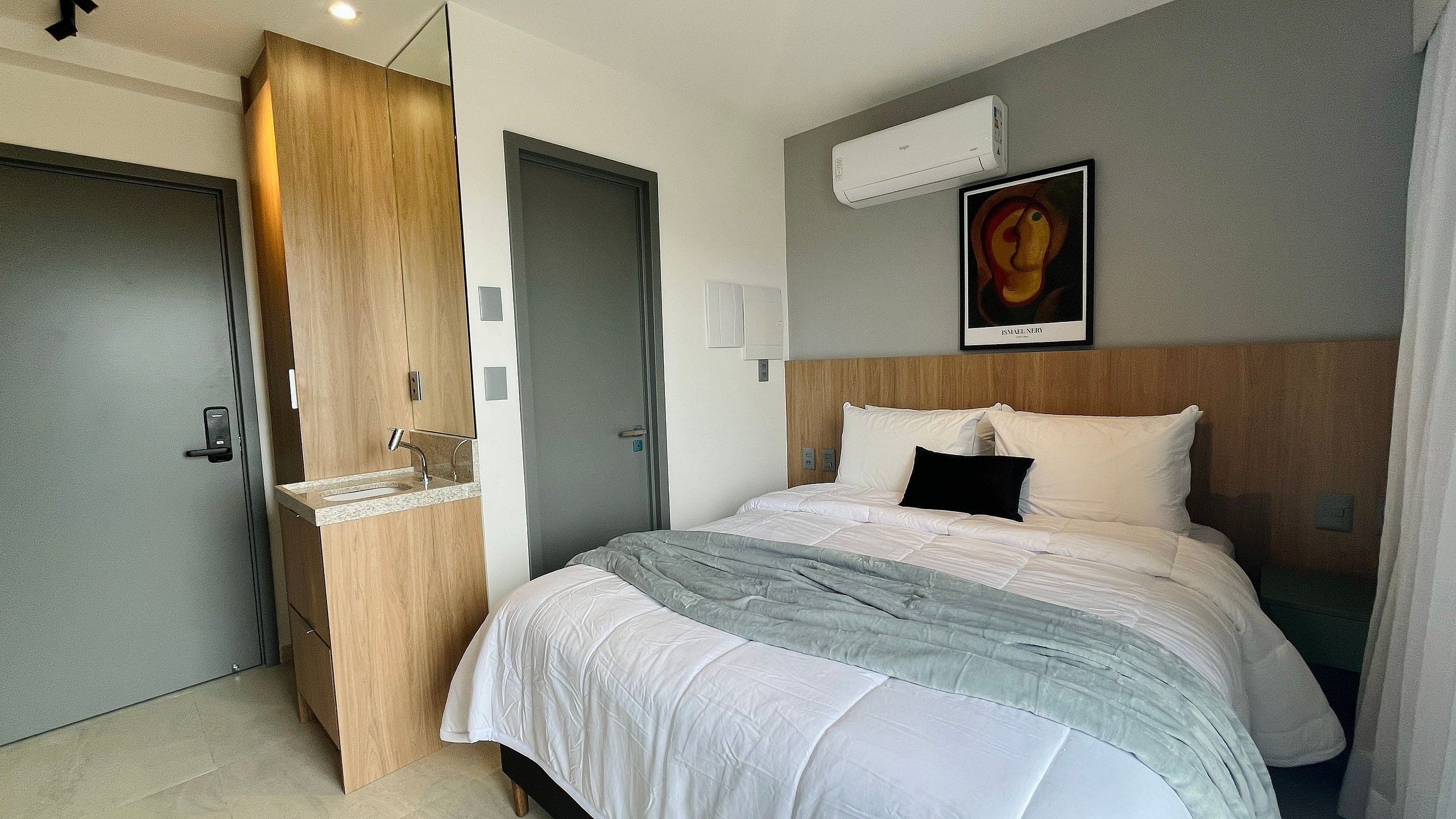 Habitación de hotel con cama, armario de madera, baño con lavamanos y aire acondicionado en la pared.