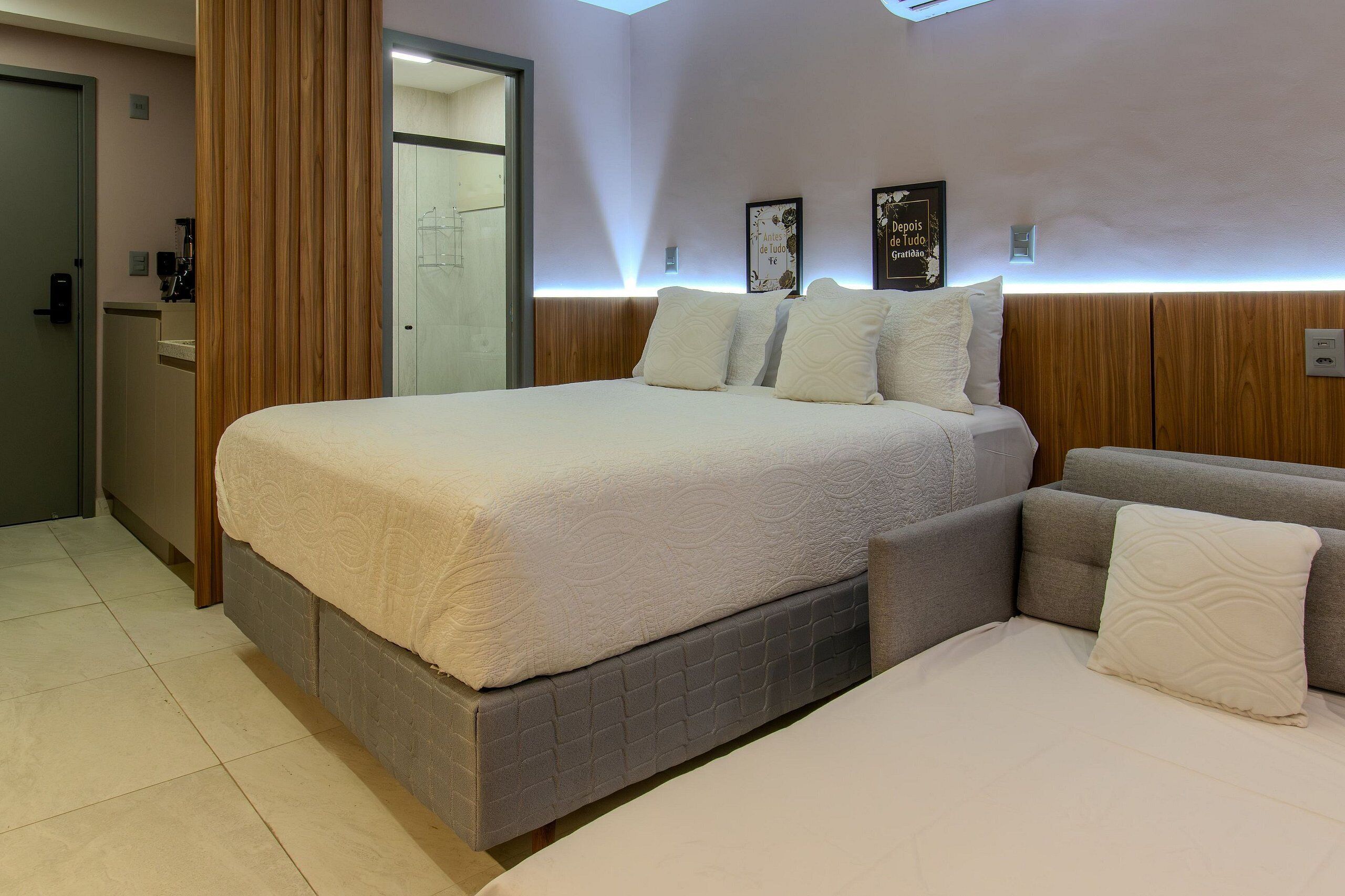 A modern bedroom with a large bed, a sofa bed, wooden paneling, and wall-mounted lighting.