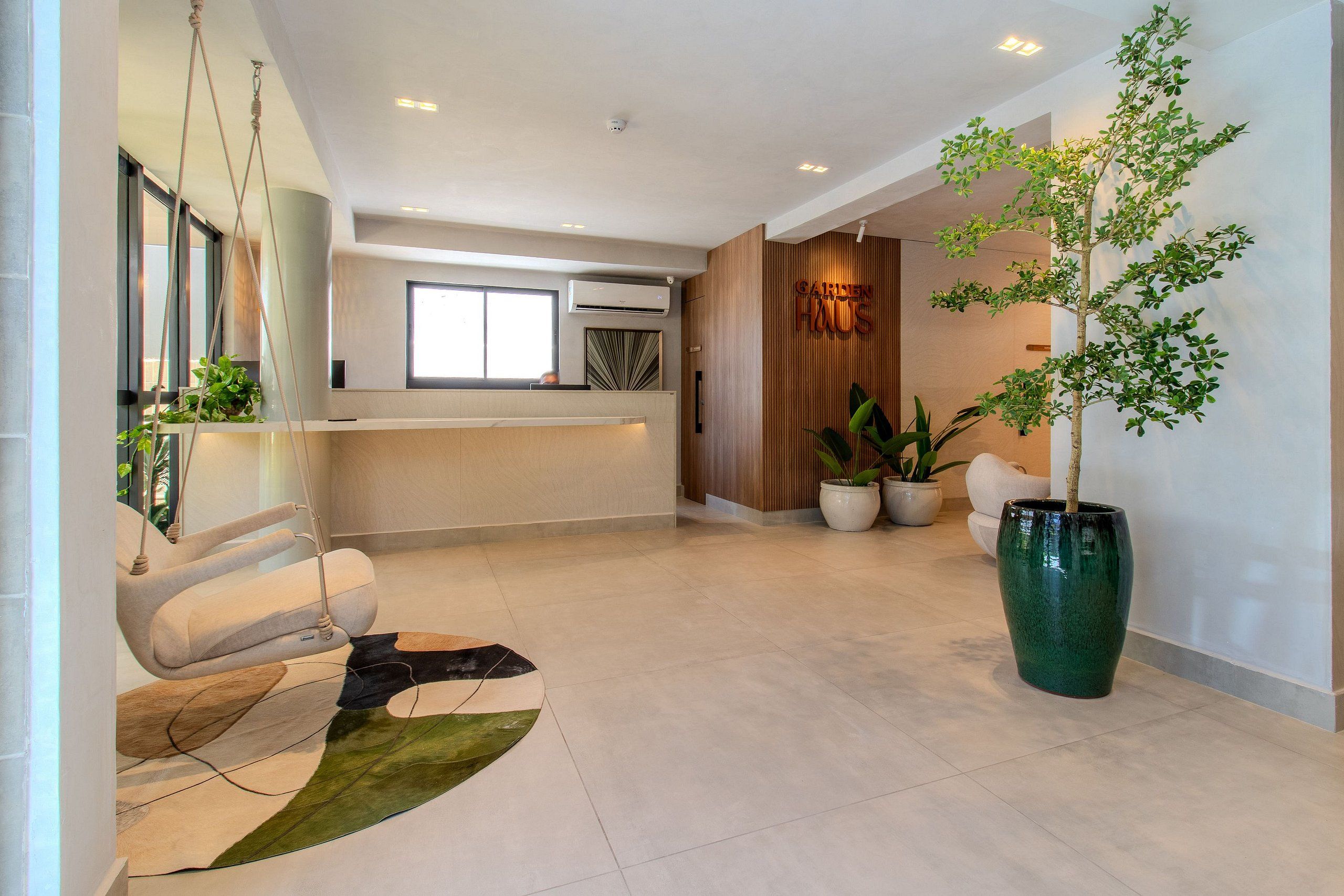 Decoração moderna com balcão de recepção, cadeira suspensa, planta verde grande e tapete contemporâneo.
