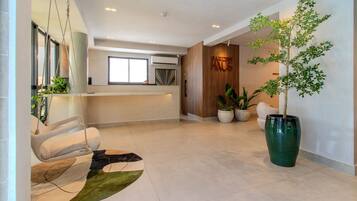 Decoração moderna com balcão de recepção, cadeira suspensa, planta verde grande e tapete contemporâneo.