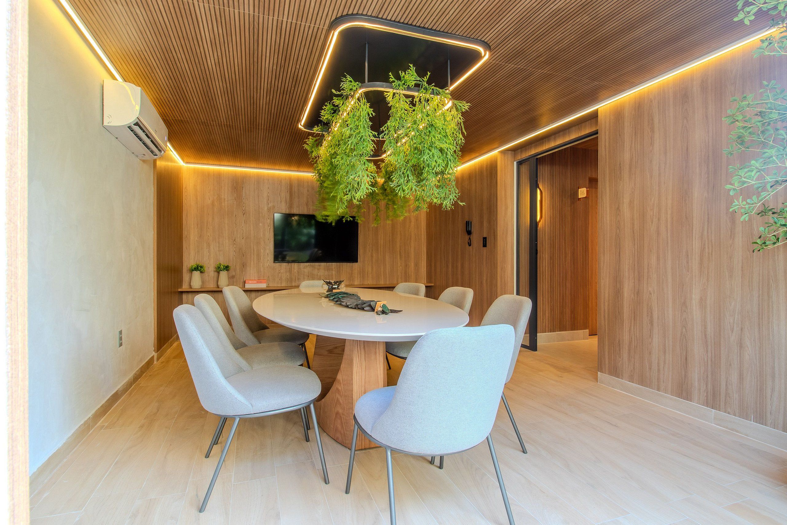 Un comedor moderno con una mesa redonda, seis sillas y una planta colgante.