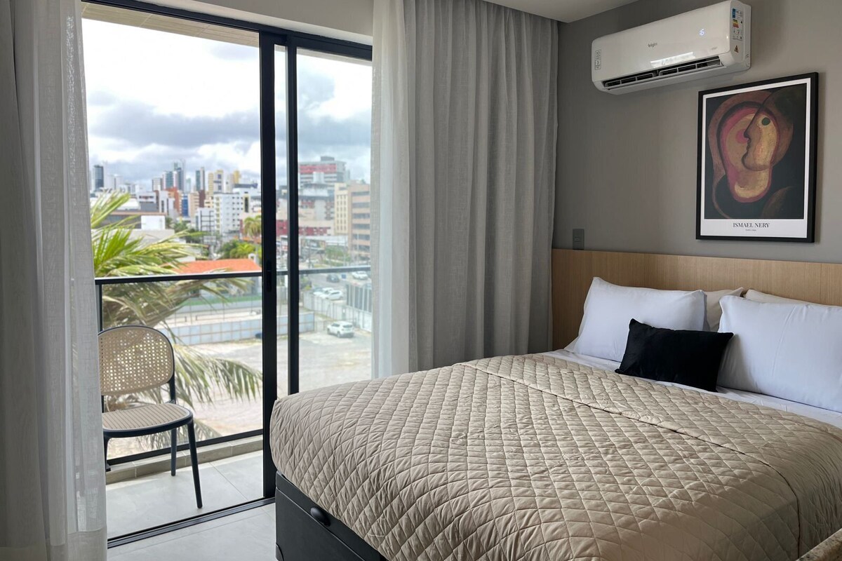 Una habitación de hotel con cama, una silla, vistas a la ciudad, aire acondicionado y un cuadro en la pared.