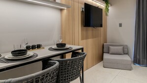 Ein moderner Essbereich mit einem Tisch, gedeckt für vier Personen, umgeben von Korbstühlen, einem grauen Sofa und einem flachbildfernseher, der an einer Holzwand angebracht ist.