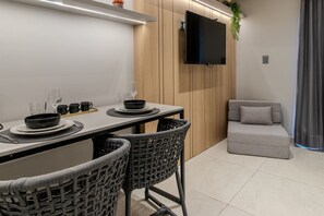 Ein moderner Essbereich mit einem Tisch, gedeckt für vier Personen, umgeben von Korbstühlen, einem grauen Sofa und einem flachbildfernseher, der an einer Holzwand angebracht ist.