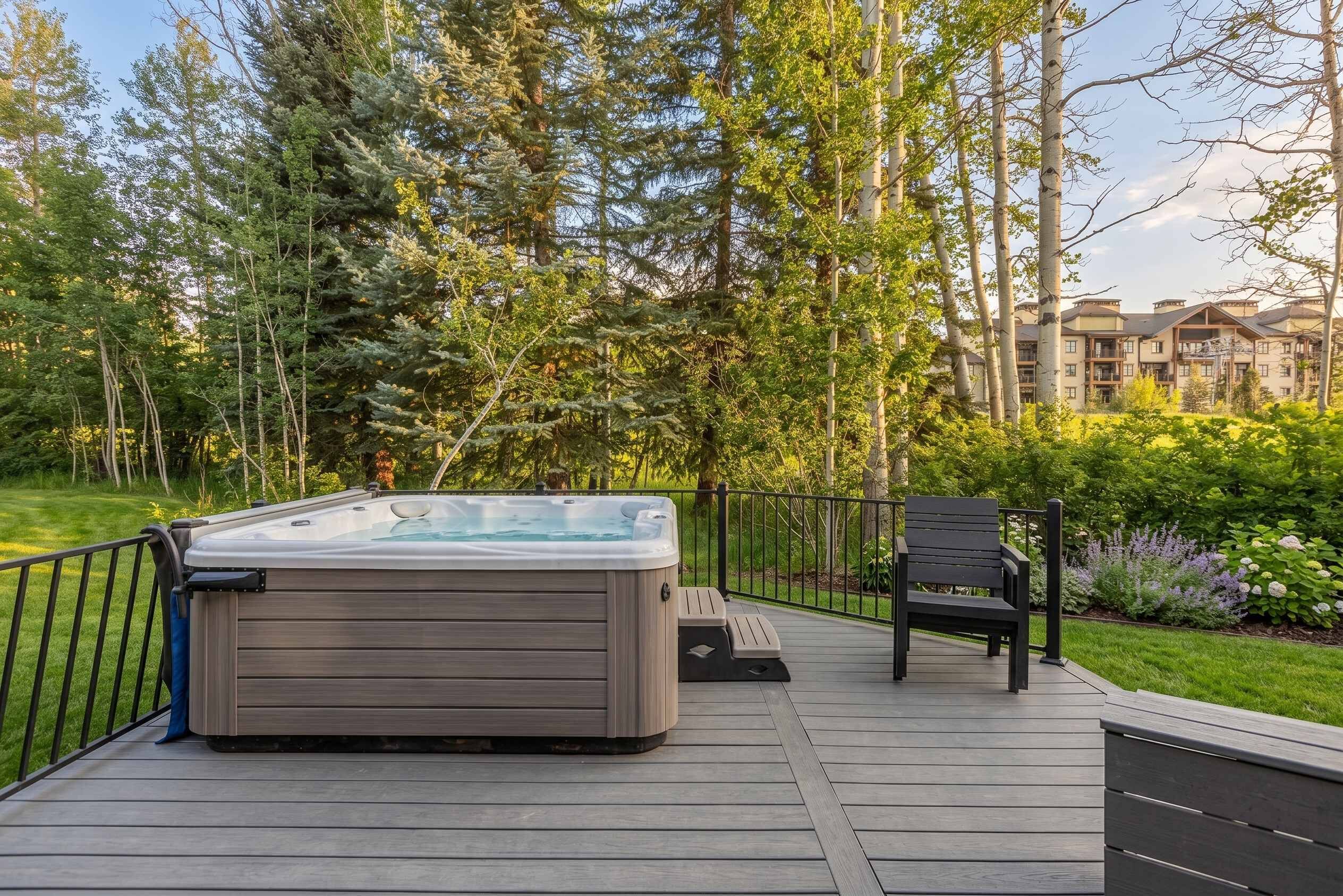 A hot tub on a wooden deck with a chair, surrounded by trees and a building in the background.