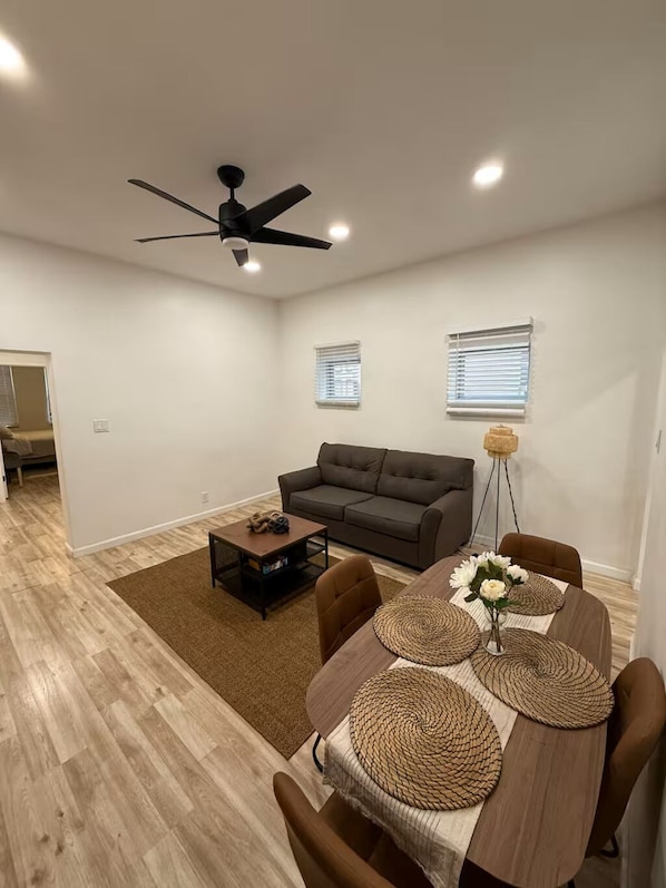 A modern living room with a sofa, coffee table, dining table with placemats, and a ceiling fan.
