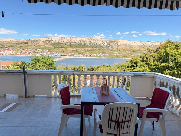 Ein Balkon mit Tisch und Stühlen, der auf eine Küstenlandschaft mit Gebäuden und Hügeln blickt.