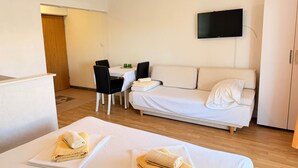 Et hotelværelse med to senge, en sofa, et spisebord og et fjernsyn.