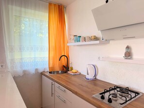 Eine Küche mit einem Gasherd, einem Spülbecken und einem Fenster mit durchsichtigem Vorhang und einem orangefarbenen Vorhang.