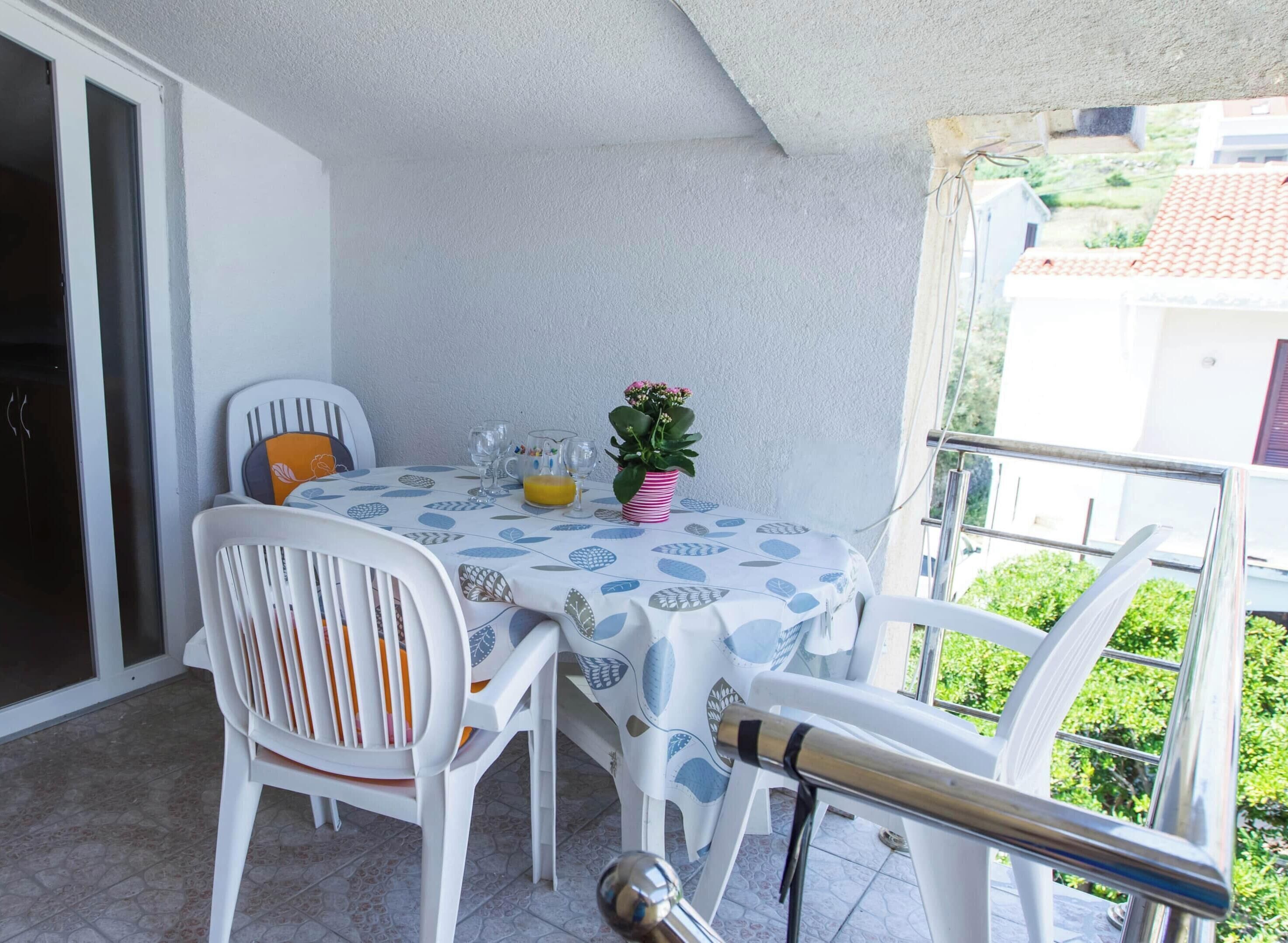 A balcony with a table set for two, a potted plant, and a glass of orange juice.