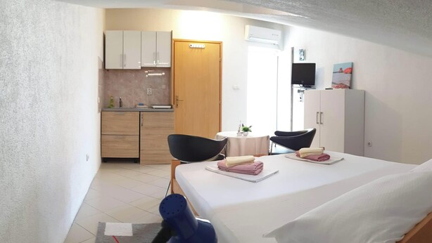 Pieni hotellihuone, jossa on sänky, työpöytä, tuoli, pieni pöytä ja taustalla pieni keittiönurkkaus.