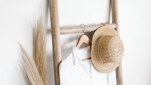 Un perchero de madera con un sombrero de paja y una camisa blanca frente a una pared blanca.
