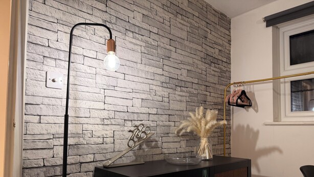 Quarto com parede de tijolos, um armário preto, um vaso de vidro com plantas secas, uma escultura de metal e um lustre.