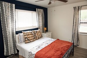 Ein Schlafzimmer mit Bett, Vorhängen, Nachttisch, Lampe und Deckenventilator.
