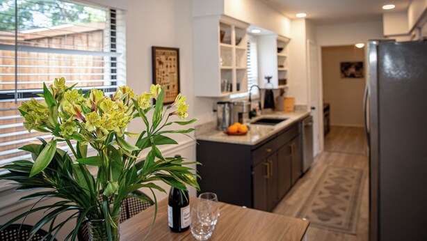 Una cocina moderna con una mesa de comedor, un florero, una botella de vino y un refrigerador.