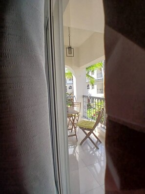 Ein Balkon mit Tisch und Stühlen, einer hängenden Leuchte und Blick auf Gebäude und Grünflächen.