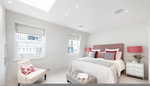 Un dormitorio con cama, mesitas de noche, una silla y ventanas amplias.