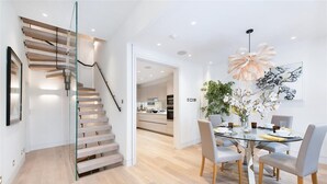 Ein modernes Interieur mit einer Glastreppe, einem Essbereich mit Glastisch und einer Küche im Hintergrund.
