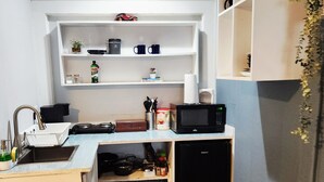 Una cucina compatta con lavandino, forno a microonde ed scaffali sopra con stoviglie e una macchinina.