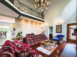 A spacious living room with a high ceiling, a staircase, a chandelier, a sofa, a coffee table, and a chair.
