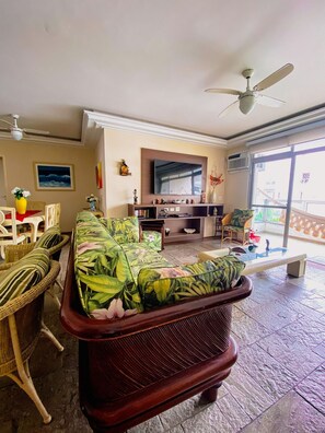 A living room with a sofa, chairs, a TV, and a ceiling fan. - Duplex w/ Pool & BBQ 500m to Enseada Beach (Guarujá)