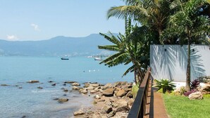 Ein hölzerner Steg führt zu einem Strand mit Palmen und Blick aufs Meer.