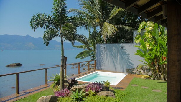 Ein Pool mit Holzterrasse, umgeben von tropischen Pflanzen und Blick aufs Meer.