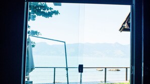 Ein Zimmer mit großem Fenster, das einen Blick auf eine Wiese und ein Gewässer mit Bergen in der Ferne bietet.