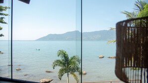 Blick durch ein Fenster auf ein ruhiges Meer mit einem Boot, Felsen und Bergen in der Ferne.