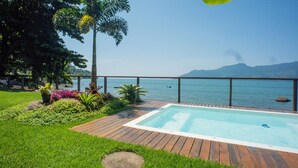 Ein Schwimmbad mit Holzterrasse, umgeben von Grün und mit Blick auf einen See und Berge.