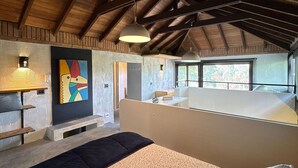 Ein geräumiges Schlafzimmer im Loft-Stil mit hohen Decken, einem großen Bett, einem Schreibtisch und Blick durch große Fenster.