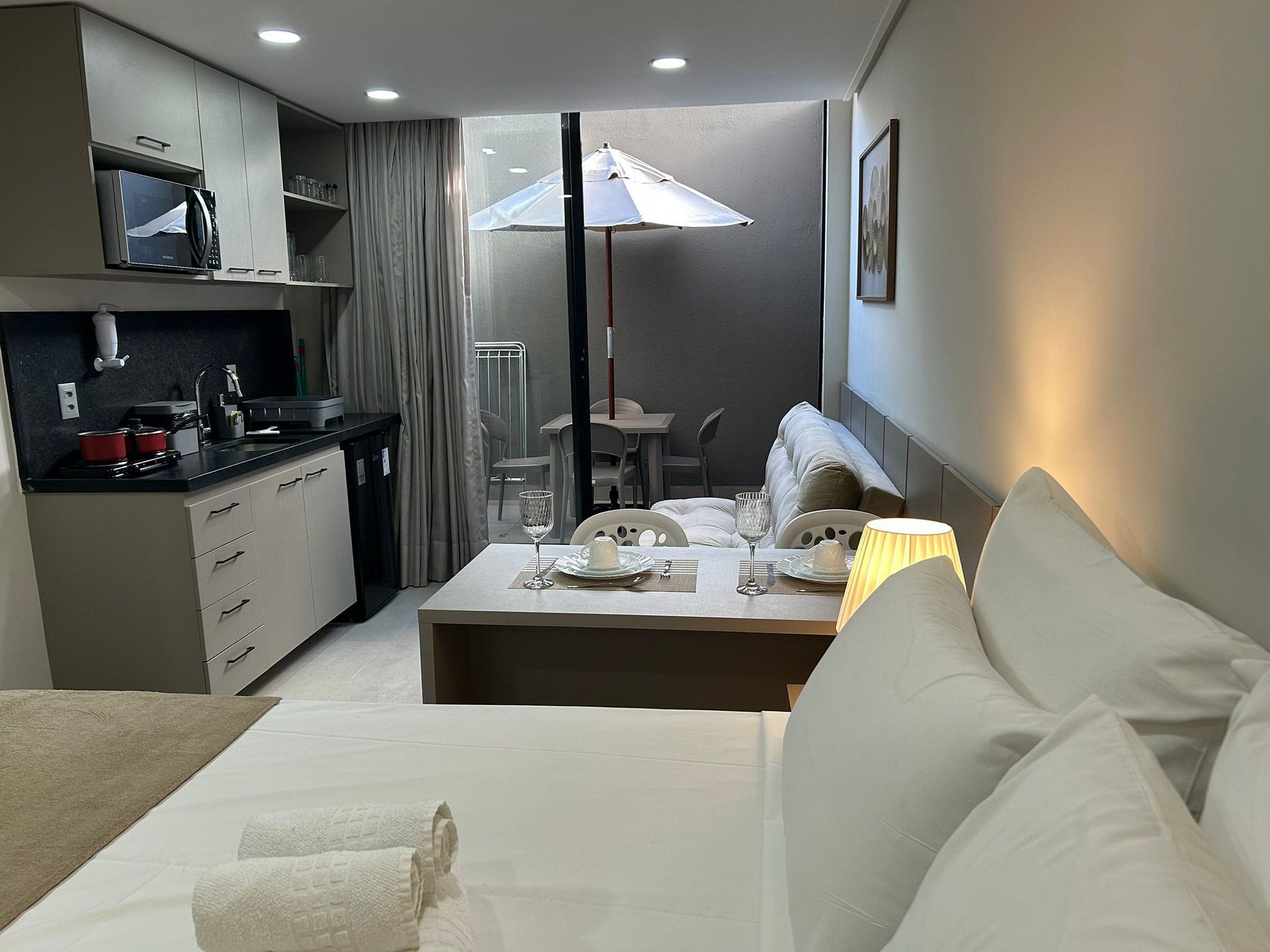 A modern hotel room with a kitchenette, a dining area, and a sofa.