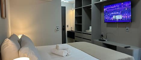 A hotel room with a bed, a TV mounted on the wall, a bedside table with a lamp, and a glass of water.