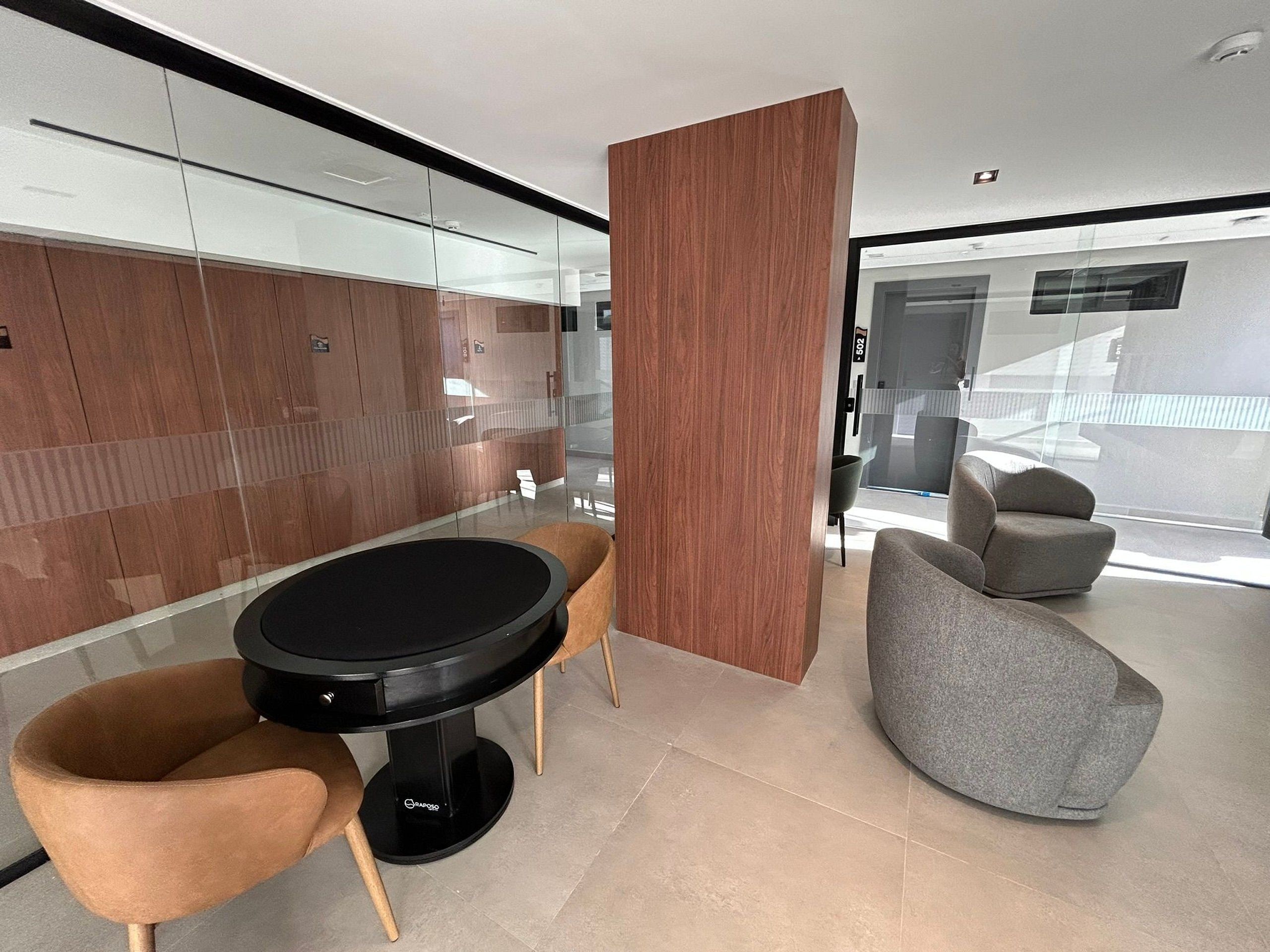 Ein modernes Interieur mit einem runden Tisch, zwei Stühlen, einer Holzwand und einem grauen Sessel.