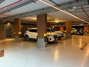 A multi-level parking garage with cars parked, columns, and overhead lighting. - Bela Hospedagem - Acqua Tambaú Flat   (João Pessoa)