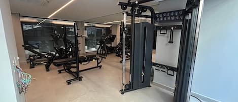 Un gimnasio con equipo de ejercicio, una banca y un espejo.