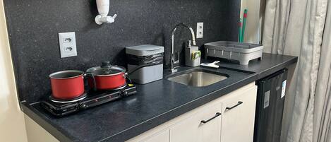 A compact kitchen with a black countertop, two red pots, a small stove, a sink, and a compact refrigerator.