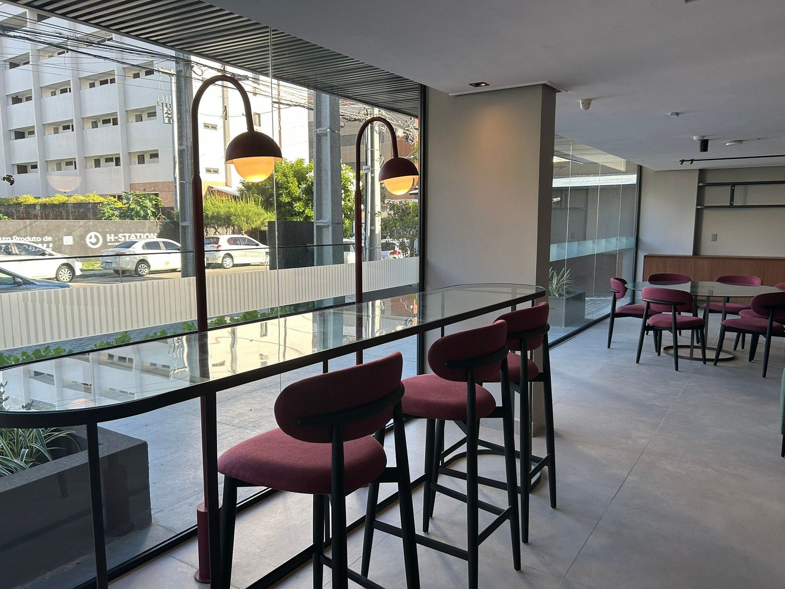 Ein modernes Interieur mit Glastrennwand, roten Barhocker und Blick auf die Straße.