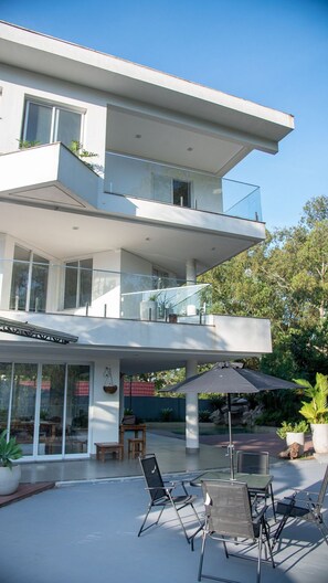 Ein modernes, zweistöckiges Haus mit überdachter Terrasse, Gartenmöbeln und einem Pool.