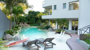 Ett modernt hus med en swimmingpool, solstolar och en trappa som leder upp till en balkong.