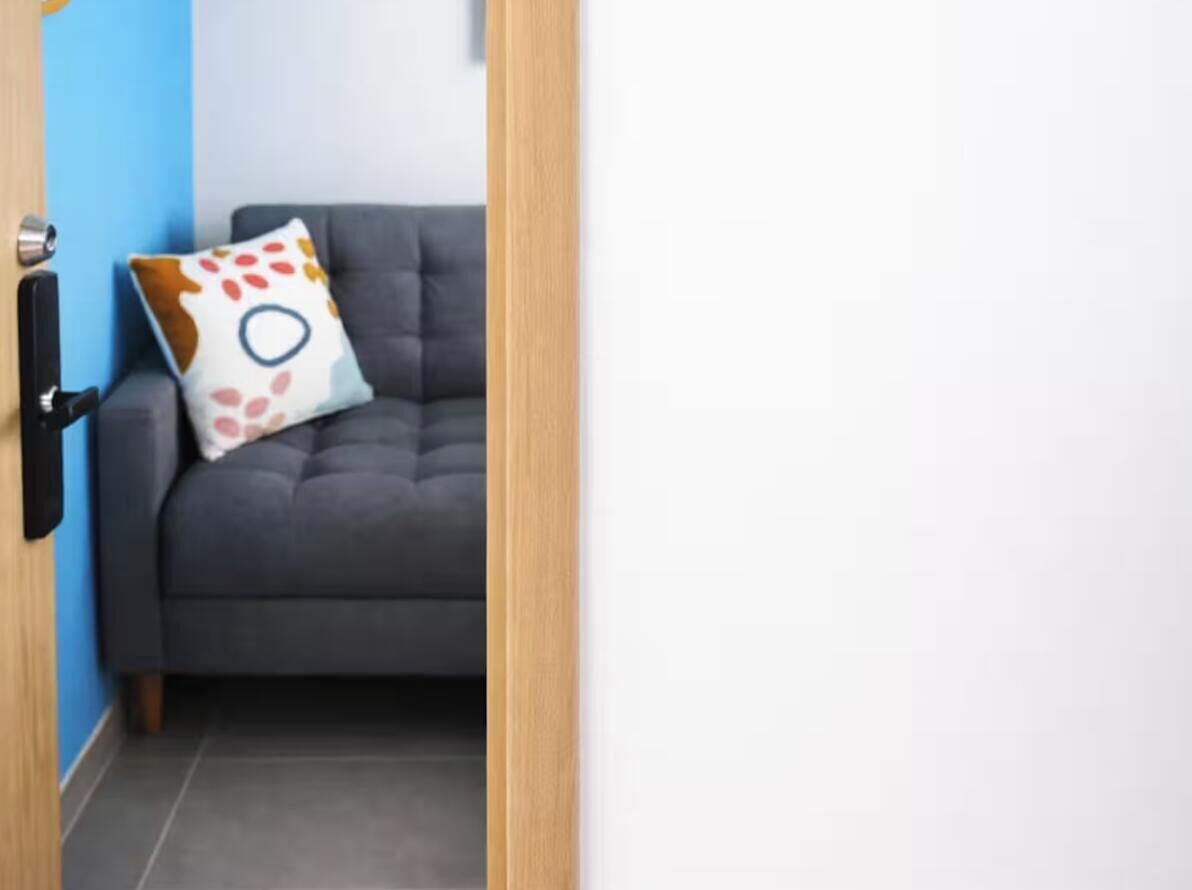 Ein Zimmer mit einem grauen Sofa, einer Holztür und einer blauen Wand.