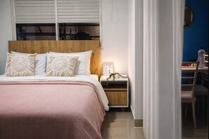 Ein Schlafzimmer mit einem Holz-Kopfteil, einem Bett mit einer rosa Bettdecke, einem Nachttisch mit einem gerahmten Bild und einem Schreibtisch mit einem Stuhl.