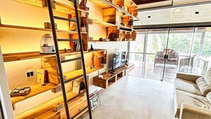 A spacious room with a high ceiling, wooden shelves, a ladder, a sofa, and a large window. - Luxury Single-Story House in Granja Viana (Jandira)