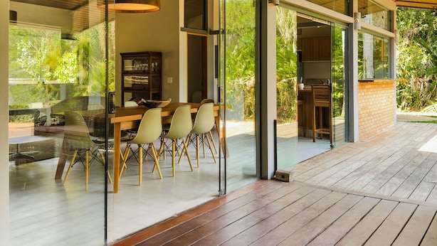 A modern house with a wooden deck, large glass windows, and a dining area with chairs and a table. - Luxury Single-Story House in Granja Viana (Jandira)